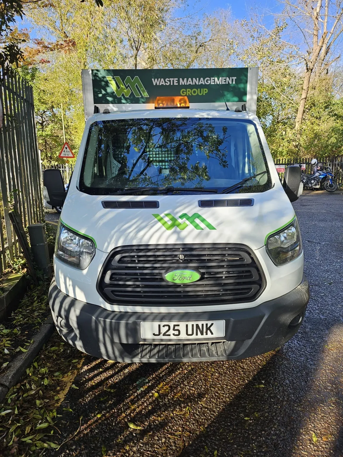 Head-on view of the front cabin of a Waste Management Group vehicle with green nature behind truck.